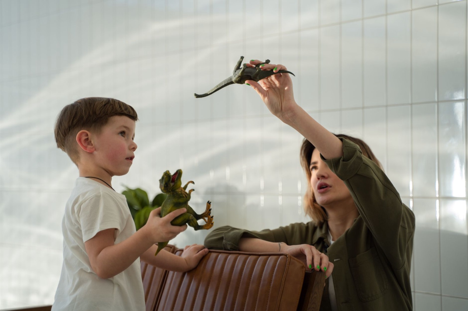 A mother and son enjoy quality bonding time playing with dinosaur toys indoors.