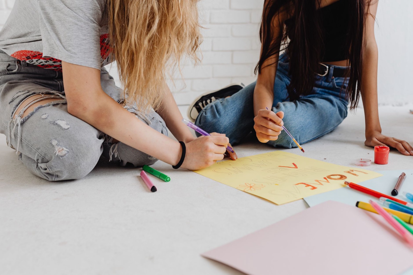 Two teenagers drawing and painting on paper, expressing creativity at home.