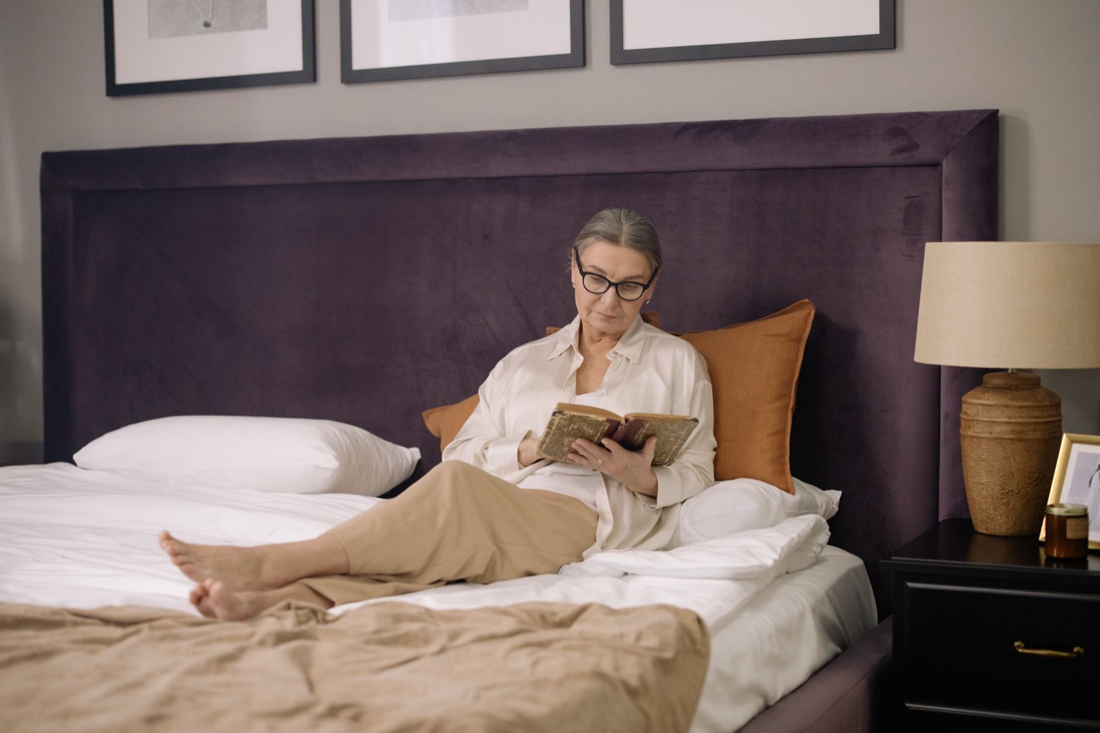A senior woman enjoys reading a book in a cozy and elegant bedroom setting.