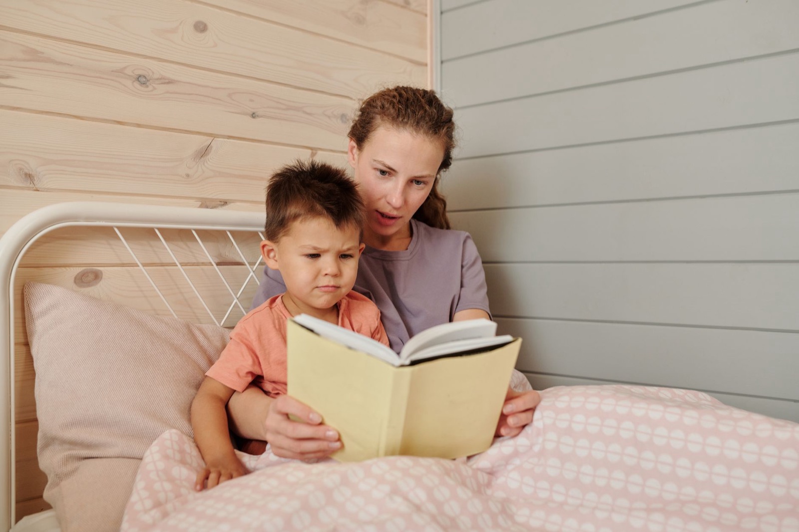 A mother and son reading a book together in a cozy bedroom setting.
