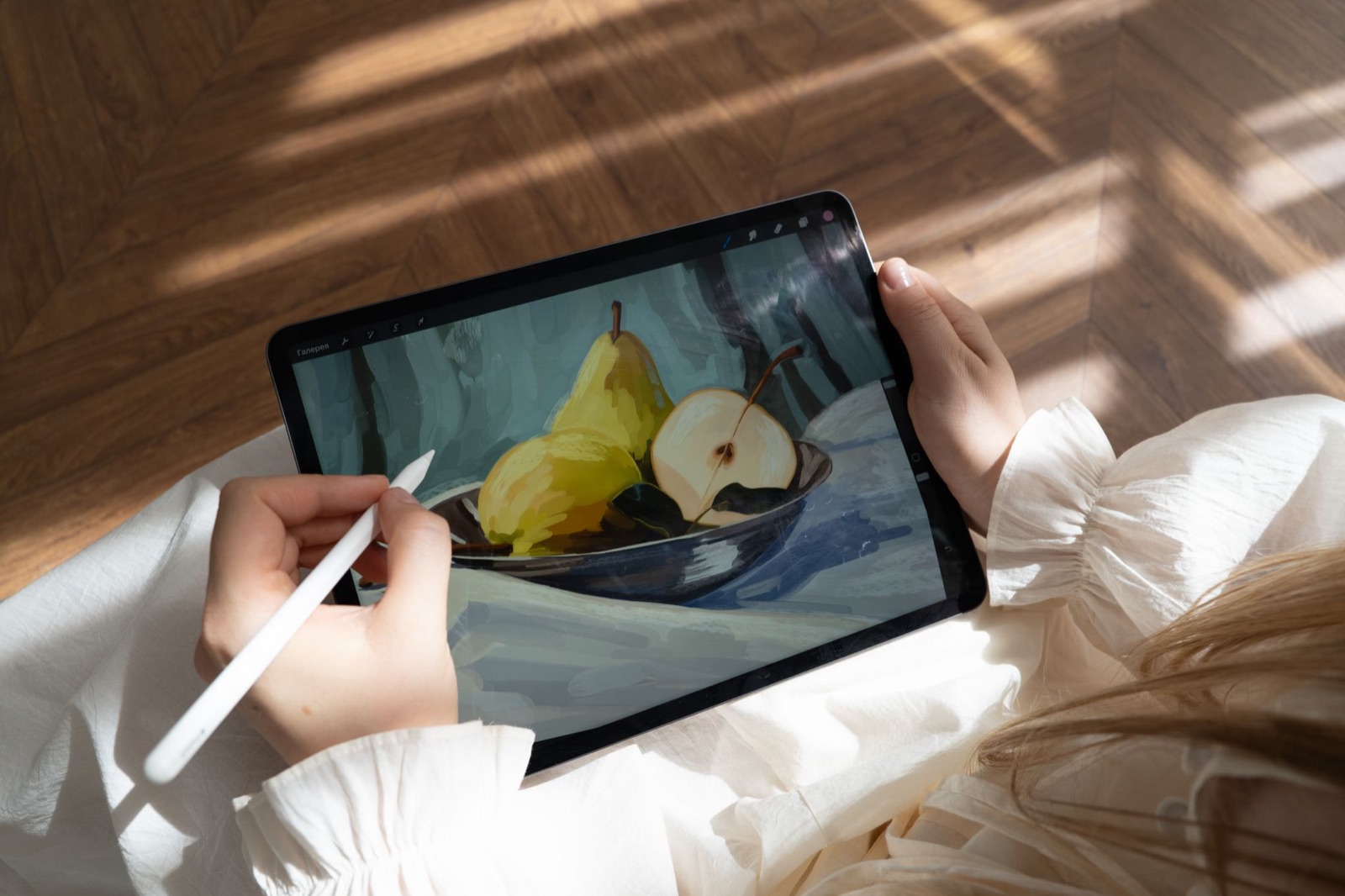 Eine Person zeichnet in einem sonnigen Raum mit einem Stift Birnen auf einem Tablet. Moderne digitale Kunst entsteht.