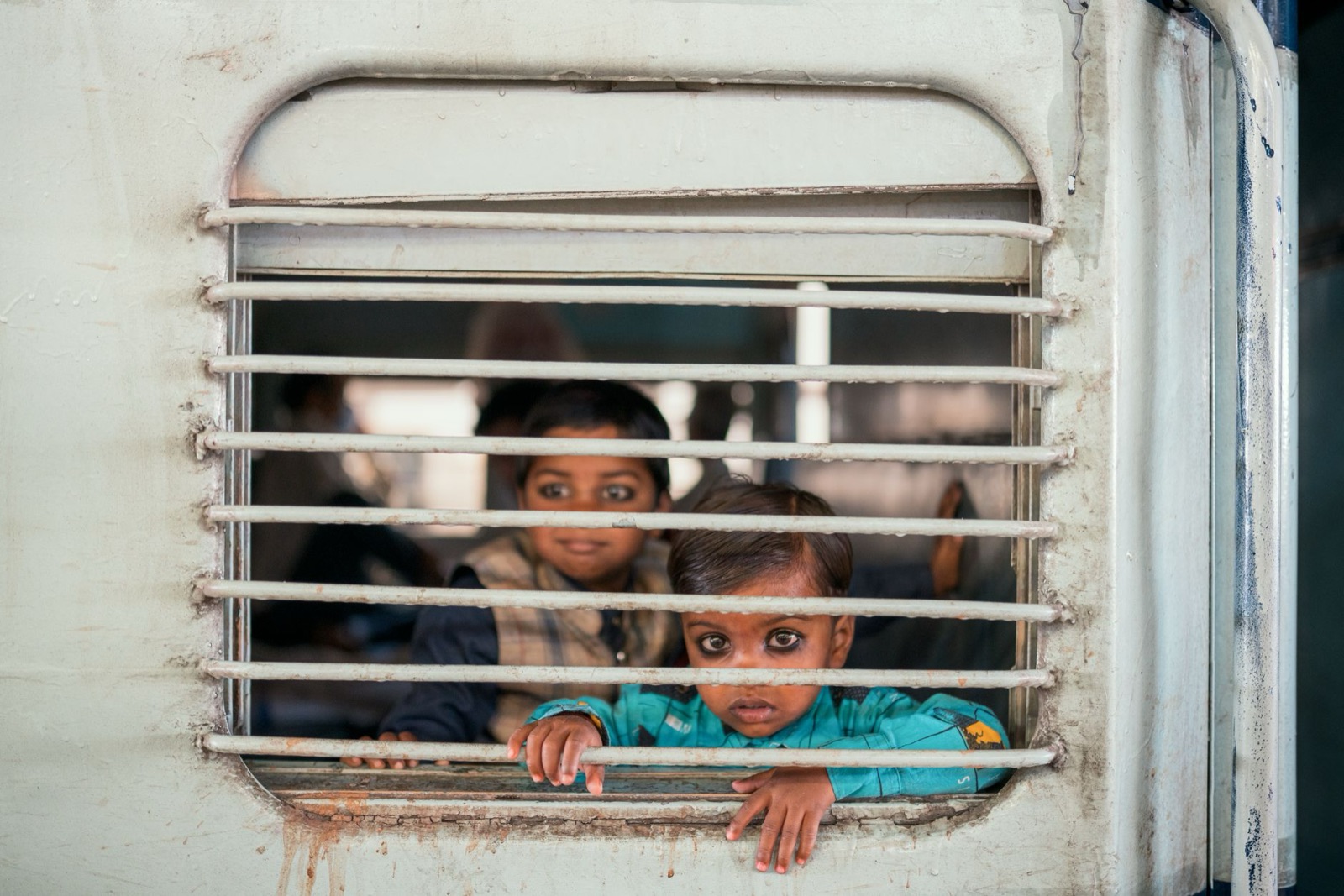 Two children curiously looking out from a train window in Delhi, India.