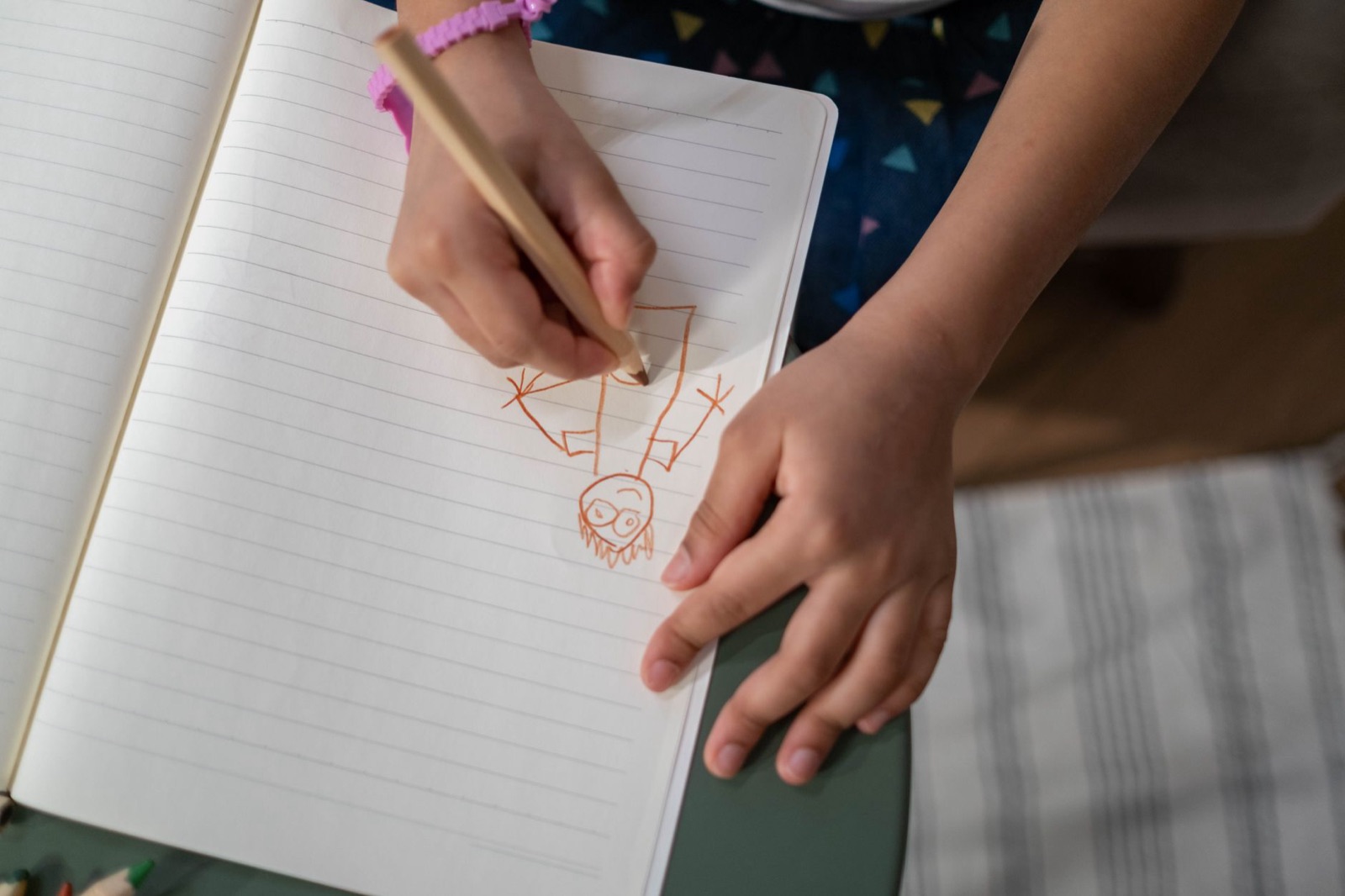 Close-up of a child's hands drawing in a notebook indoors.