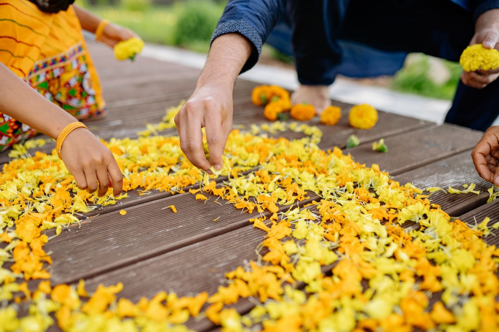 Hands arranging vibrant yellow flower petals for Diwali decoration outdoors.