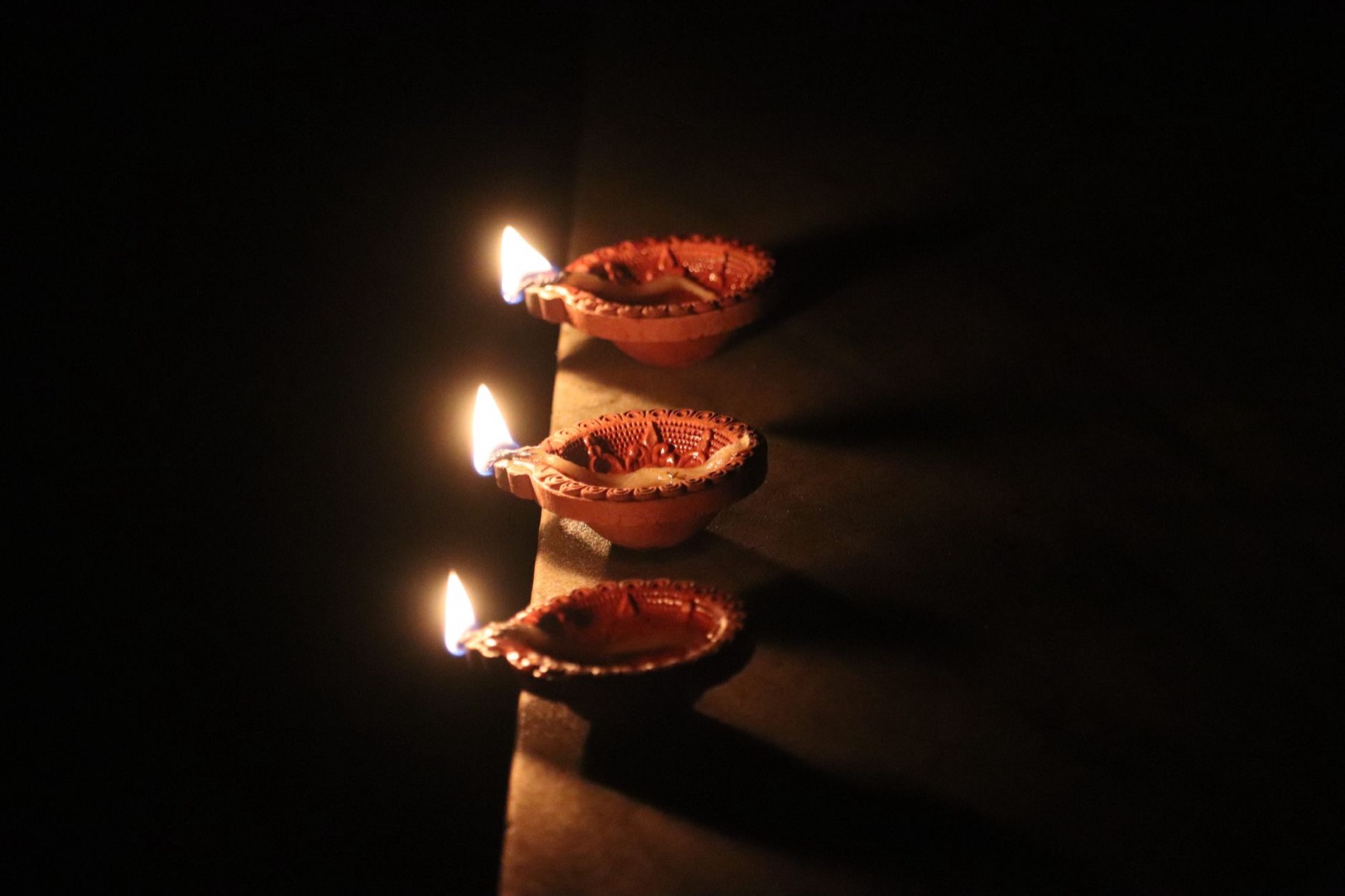 Three clay lamps lit during Diwali casting a warm glow in the darkness.