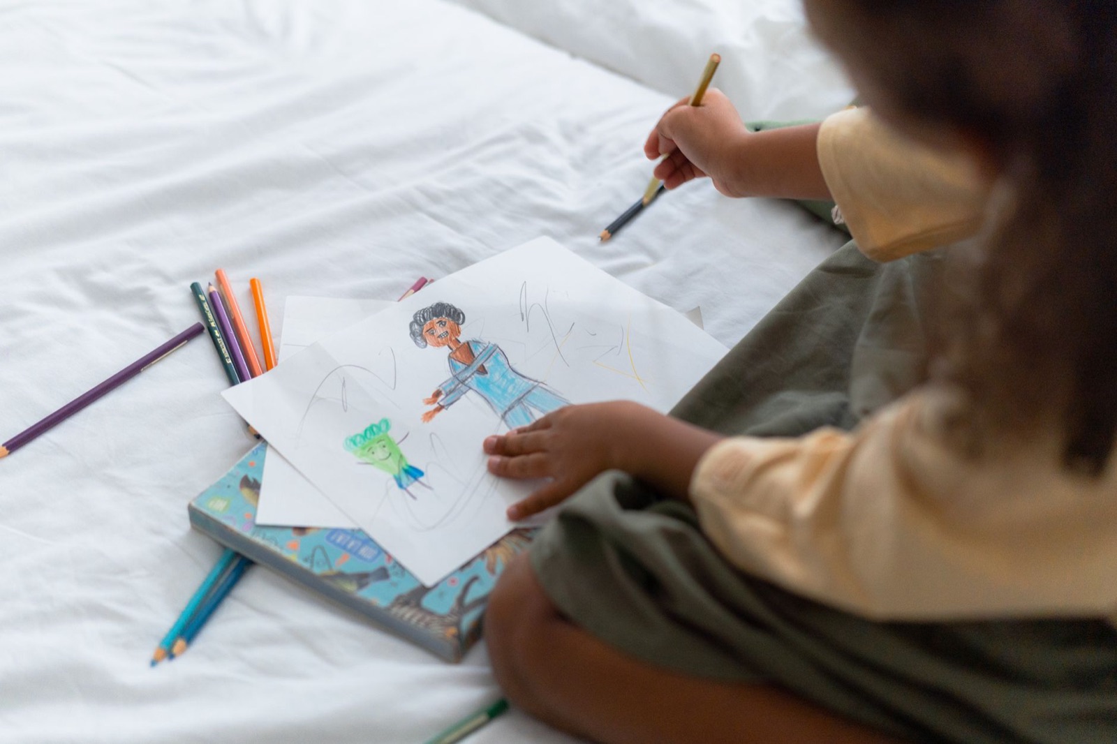 A young child creatively drawing with colored pencils at home, showcasing artistic expression.