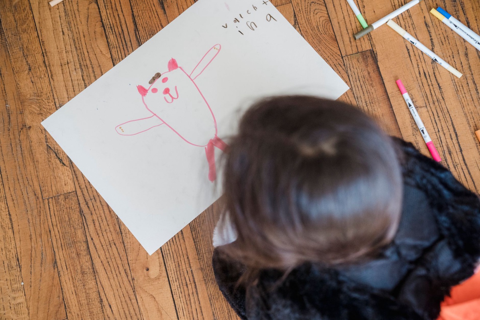 A young child draws on paper with crayons on a wooden floor. Creative playtime.