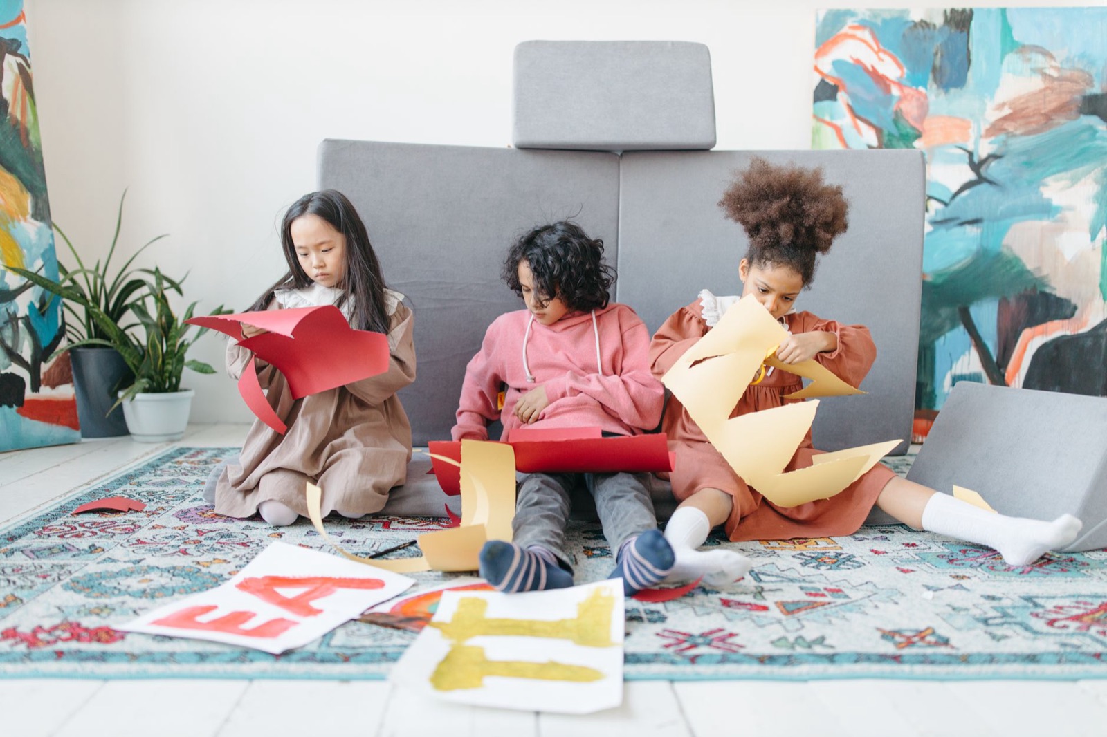 Three children creating art with colored paper indoors, showcasing teamwork and creativity.
