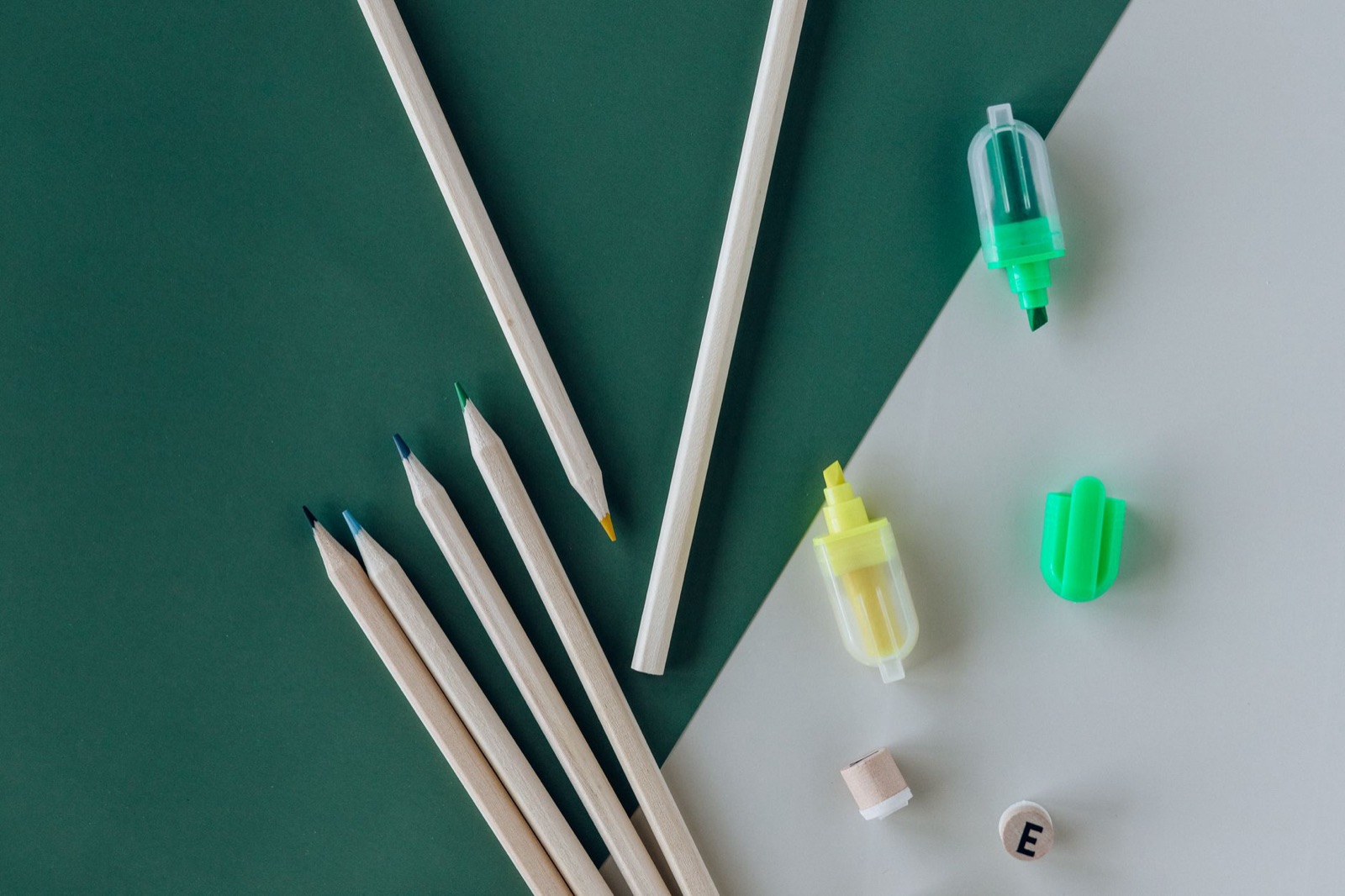 Art supplies including pencils and highlighters on a green and white background, perfect for creative projects.