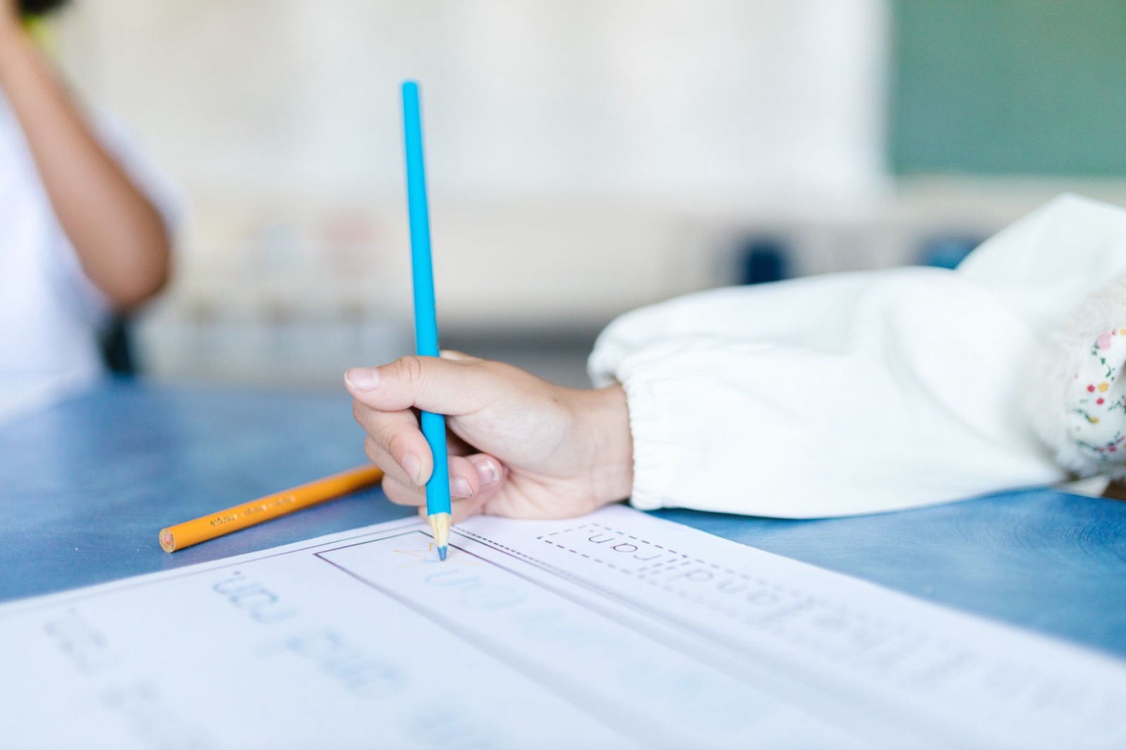A child writes on paper with colored pencils, enhancing fine motor skills in a classroom setting.