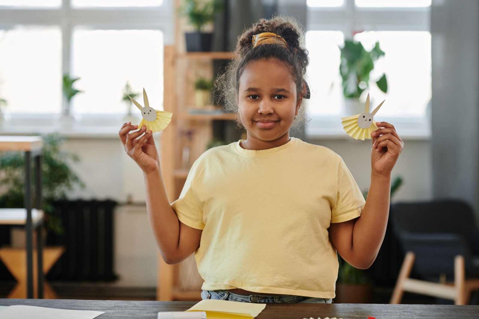 Young girl presenting paper crafts in a bright indoor setting, showcasing creativity and learning.