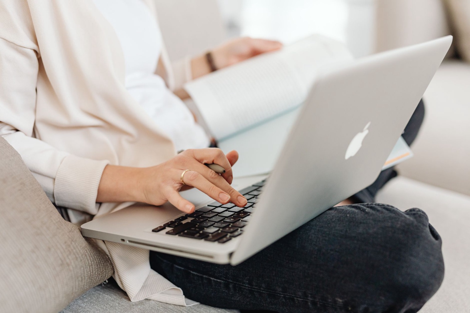 Close-up of a person multitasking, typing on a laptop while holding a book on their lap.