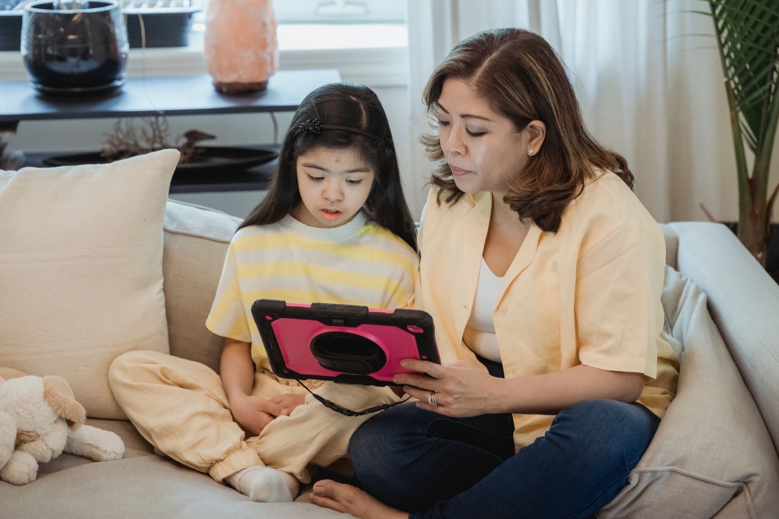 A mother and daughter bonding on the sofa using a tablet indoors.