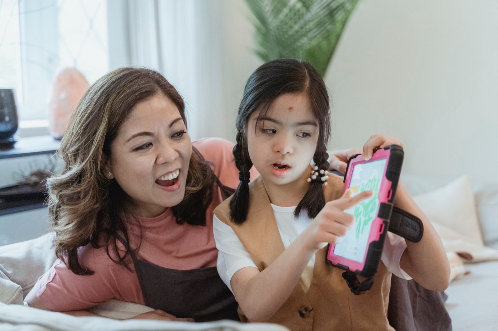Mãe e filha aproveitando o tempo juntas, usando um tablet dentro de casa.