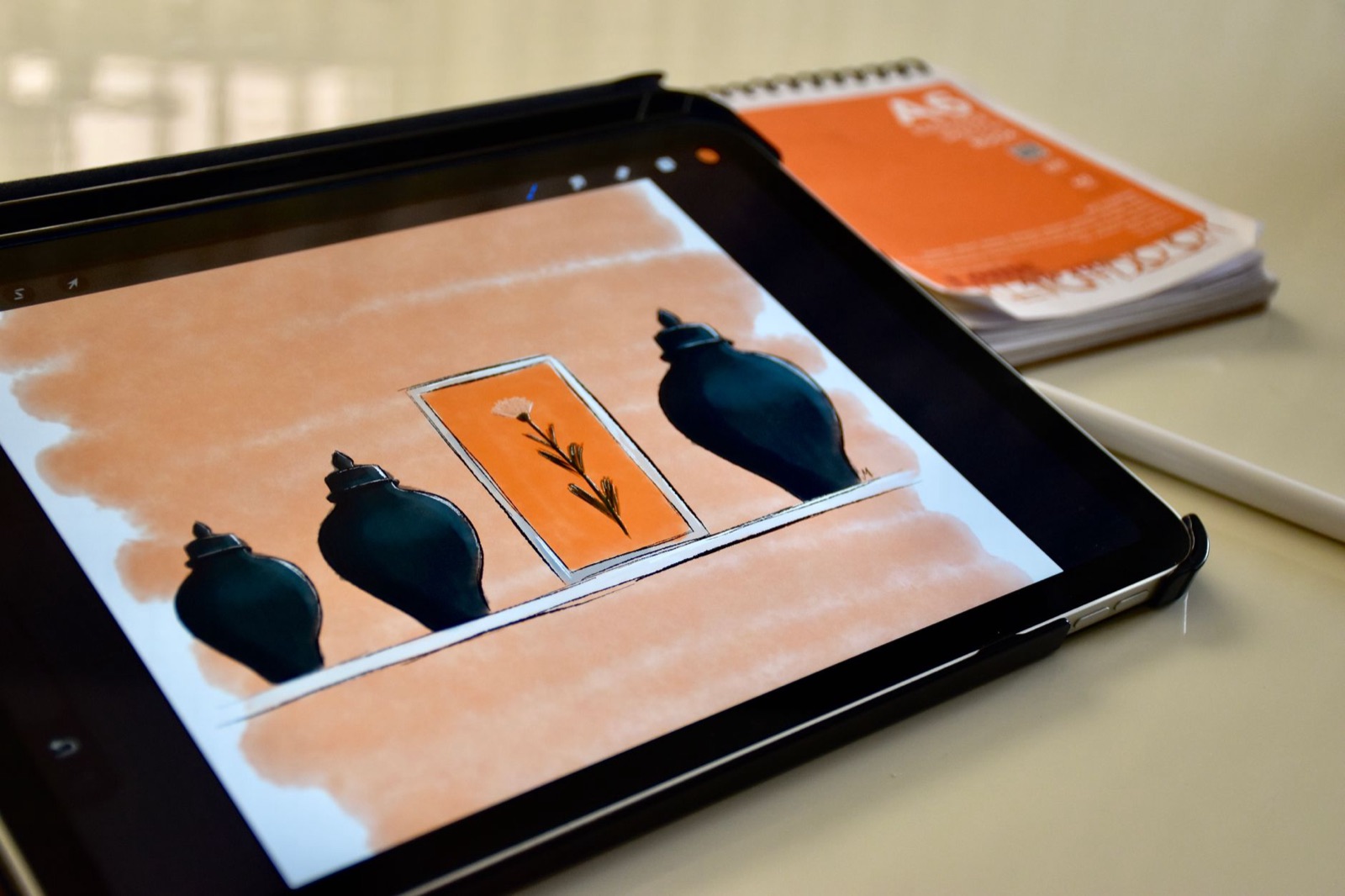 Um esboço digital de vasos e uma flor na tela de um tablet, com uma caneta stylus e um caderno ao lado.