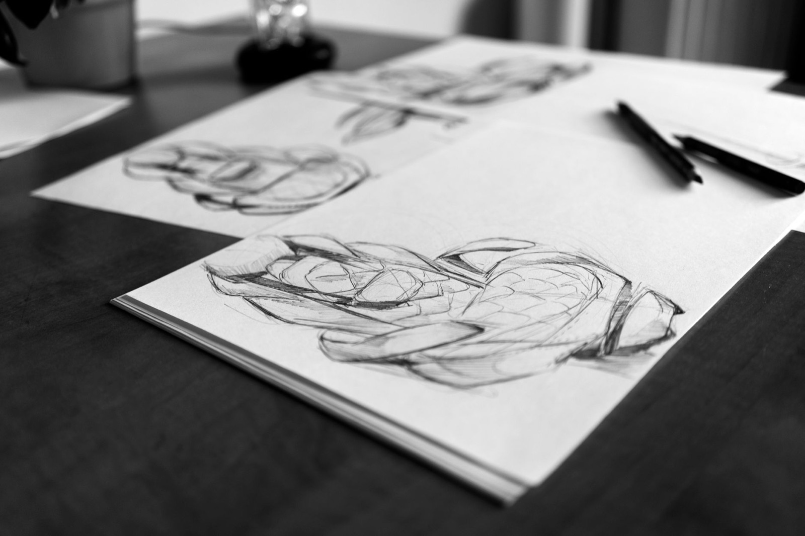 Imagem em preto e branco de esboços em papel e lápis sobre uma mesa de madeira.