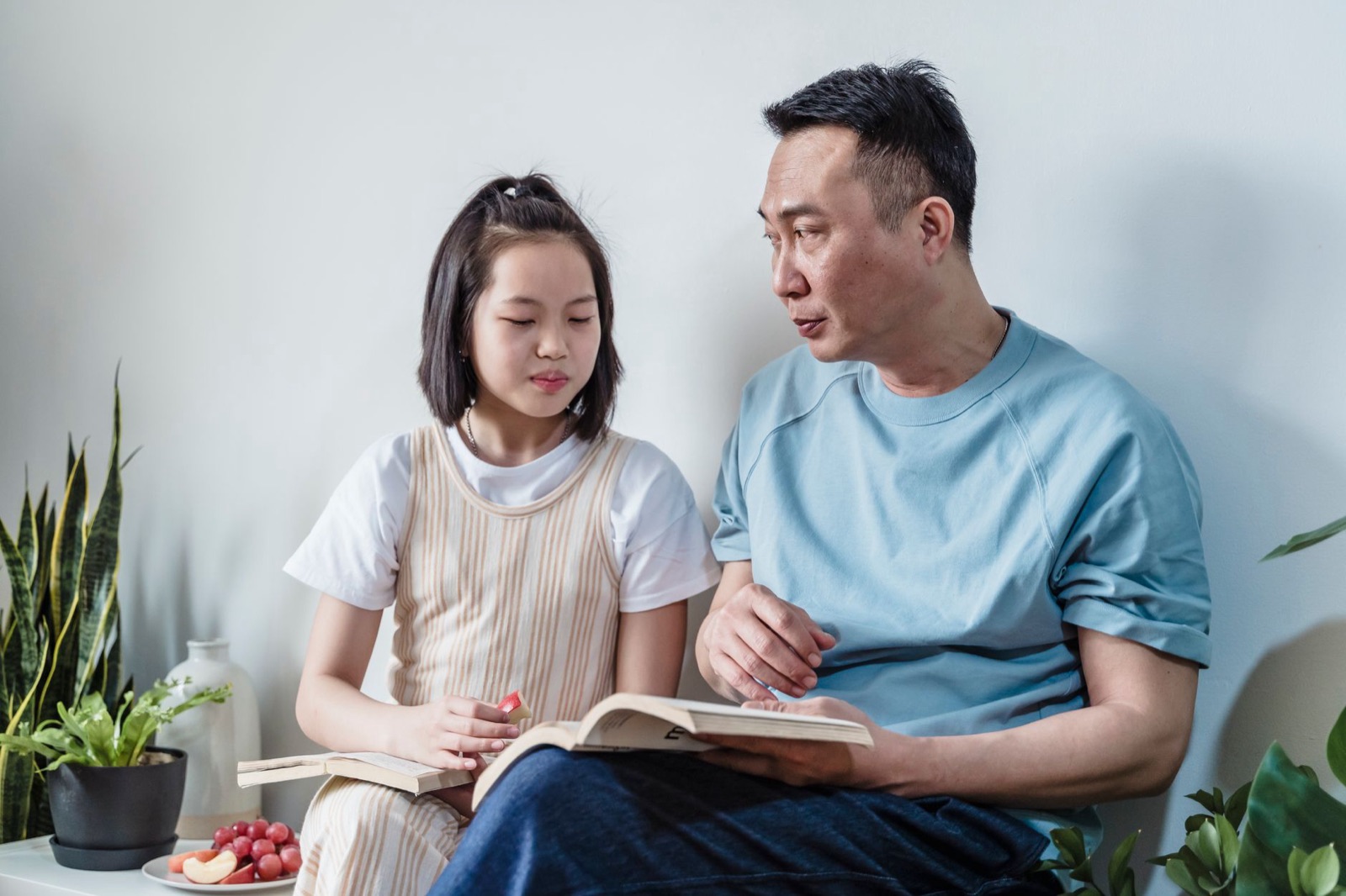 Father and daughter enjoying a reading session together at home, surrounded by plants.