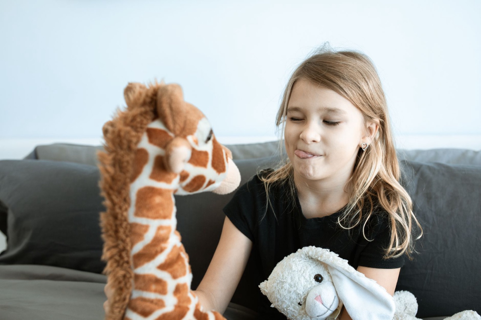 A young girl joyfully interacts with stuffed animals in a cozy indoor setting, showcasing playful childhood moments.
