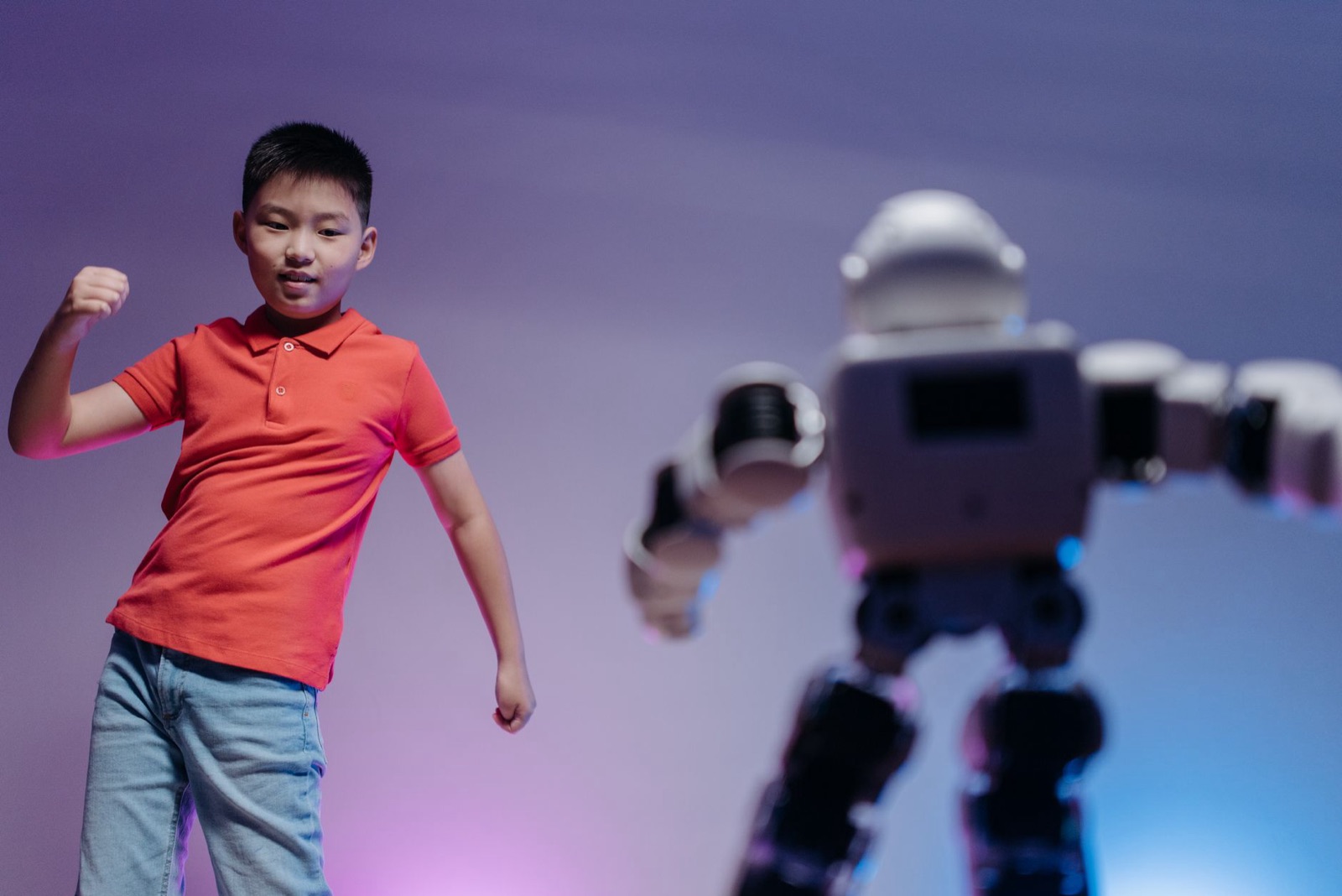 Ein kleiner Junge in rotem Hemd tobt unter buntem Licht vor einem futuristischen Spielzeugroboter.