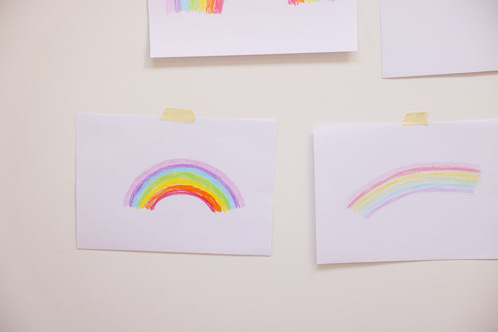 Hand-drawn rainbow art on paper taped to a white wall, showcasing creativity.
