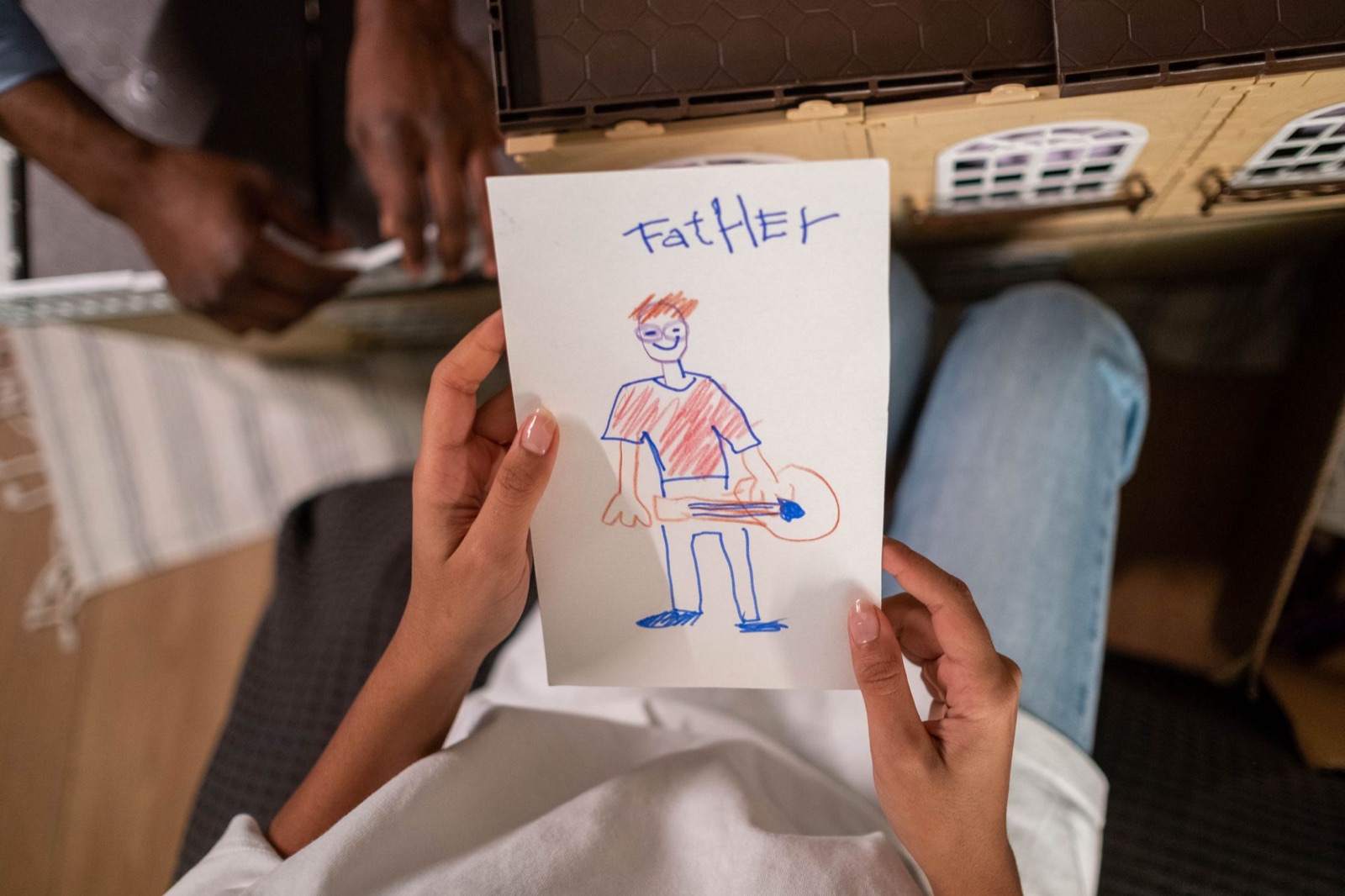A high-angle view of a child's drawing of their father, placed in front of a toy house, showing family creativity.