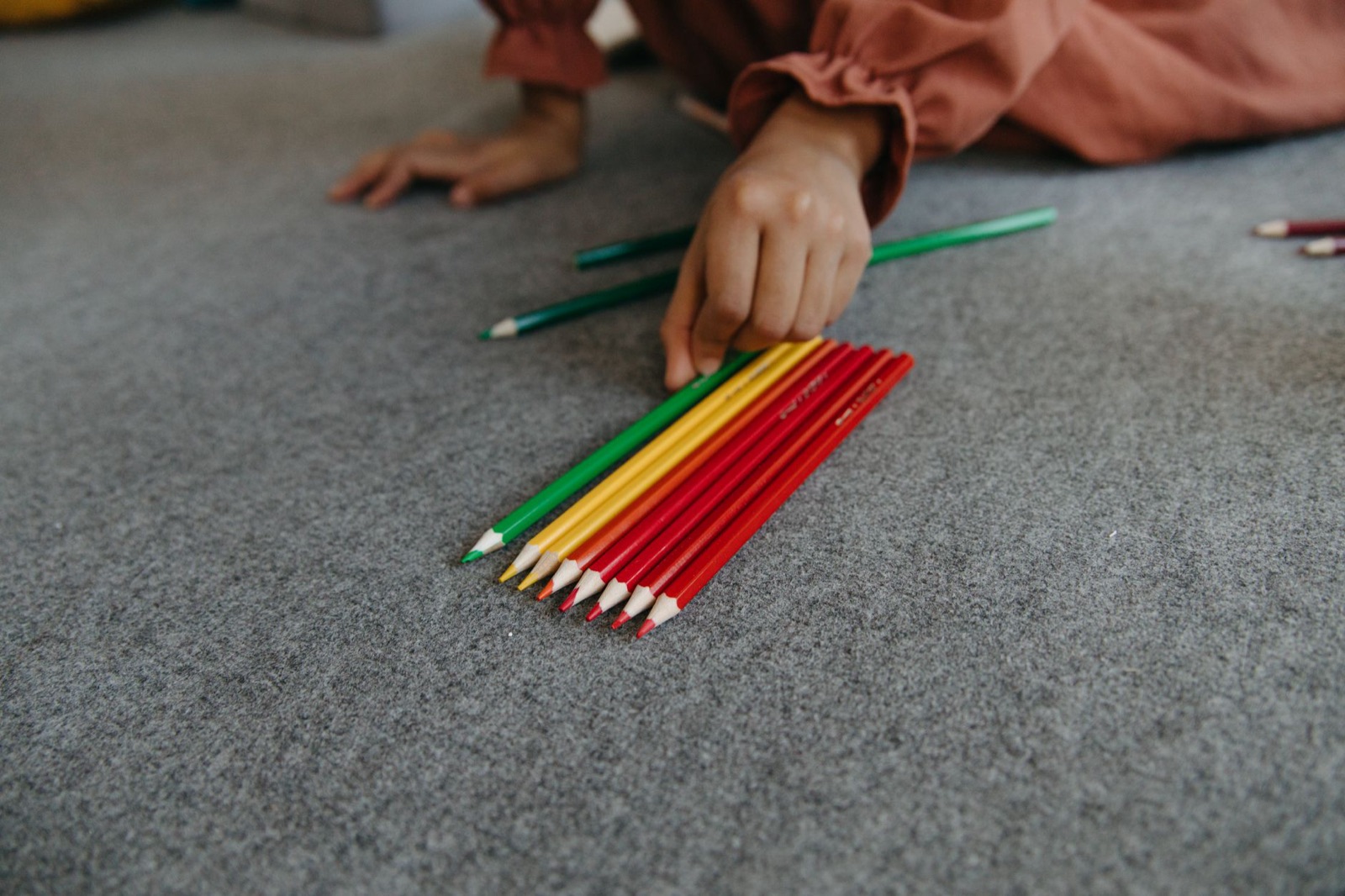 A hand organizes vibrant colored pencils on a carpeted floor.