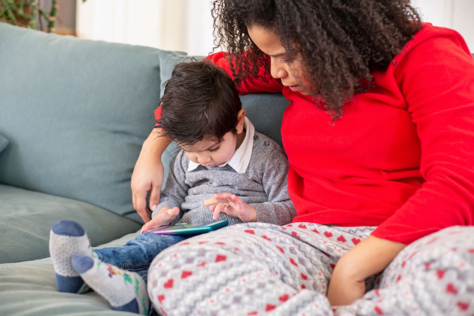 A mother and child bonding on a sofa using a tablet device indoors.
