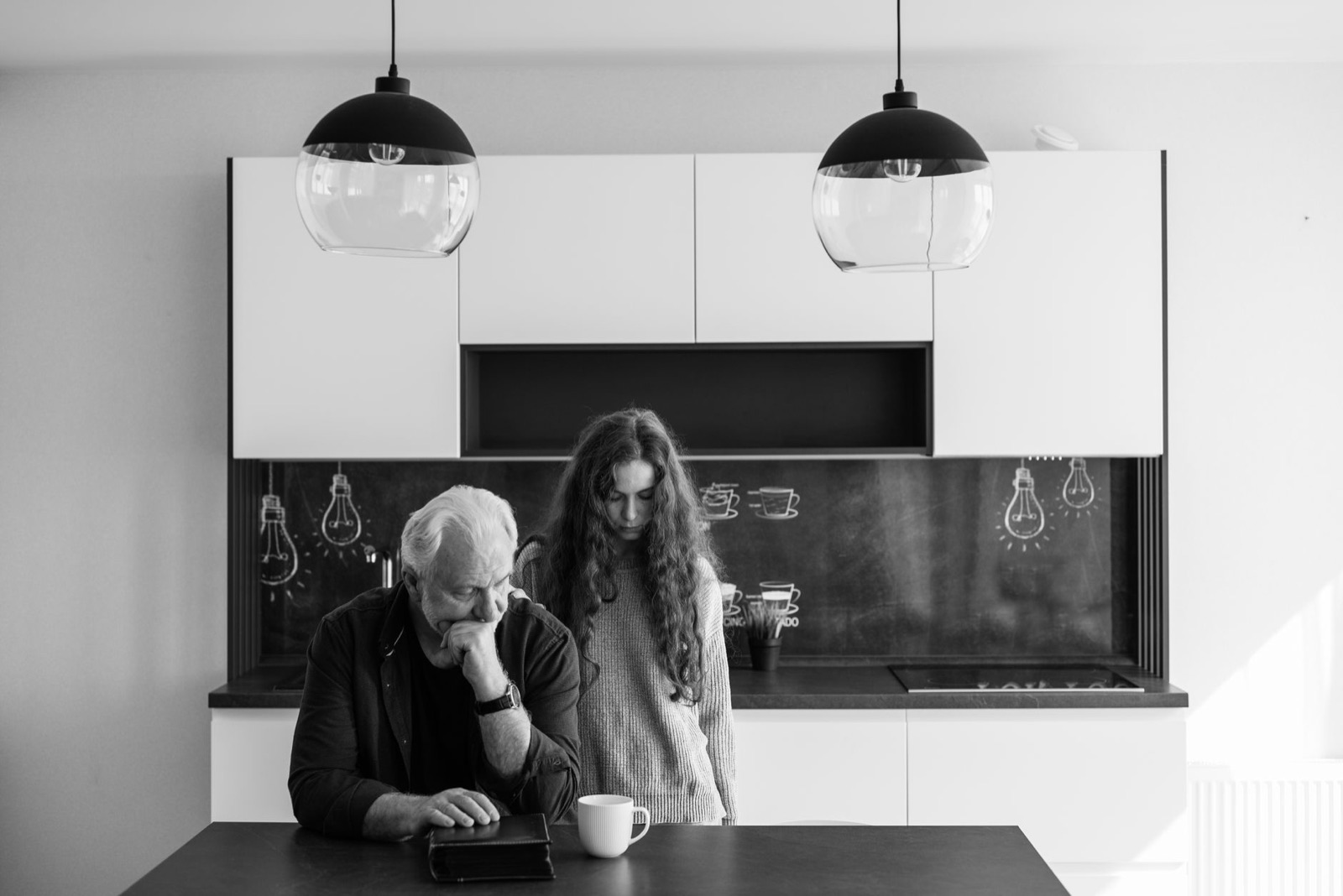 A father and daughter sharing a pensive moment in a modern kitchen setting.