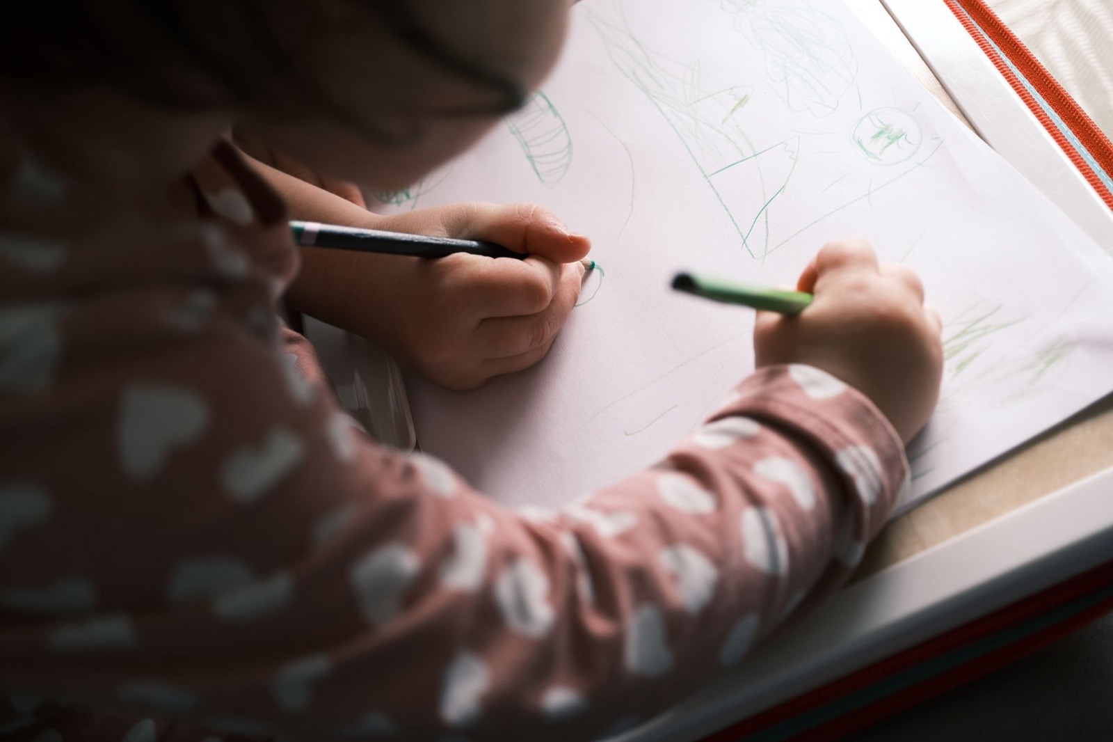 A young child drawing with colored pencils, capturing creativity and concentration in soft lighting indoors.