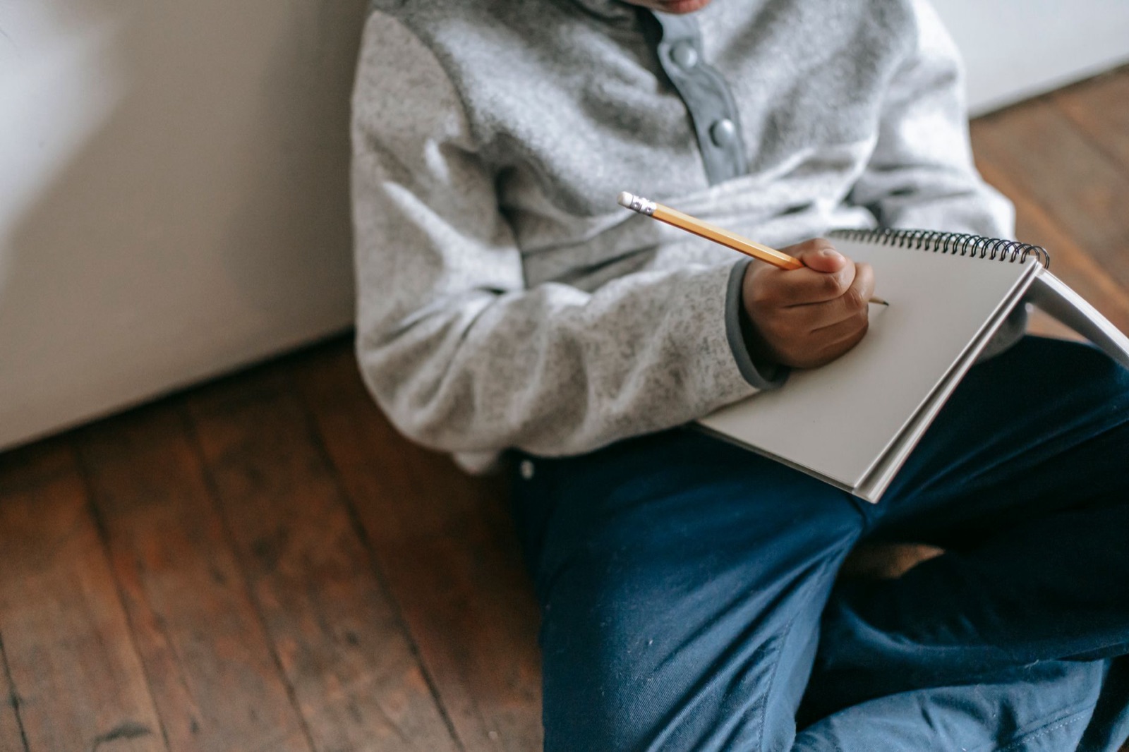 From above faceless child with pencil and notebook taking notes while sitting on floor