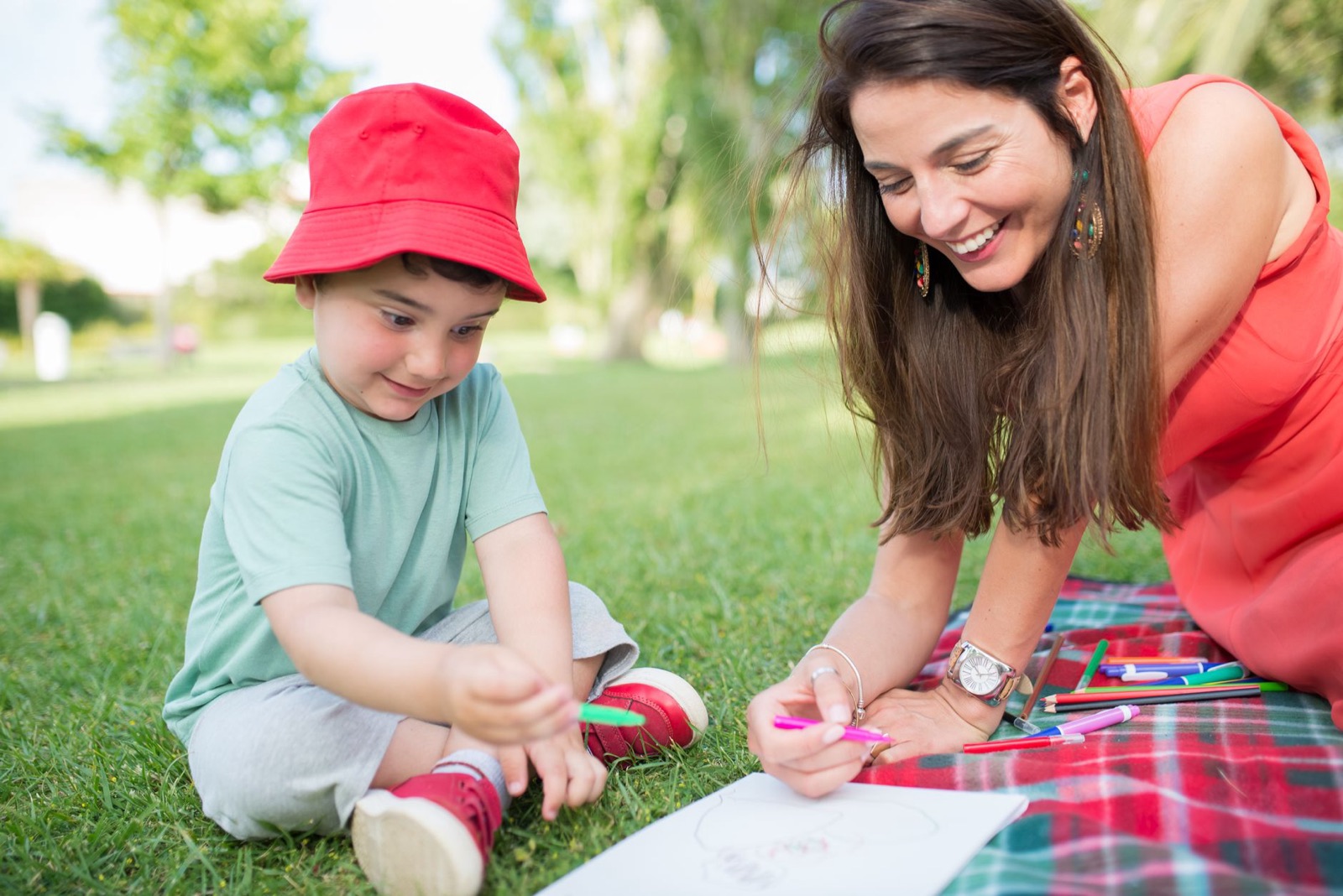 A joyful moment of a mother and child drawing on a picnic in a sunny outdoor setting.