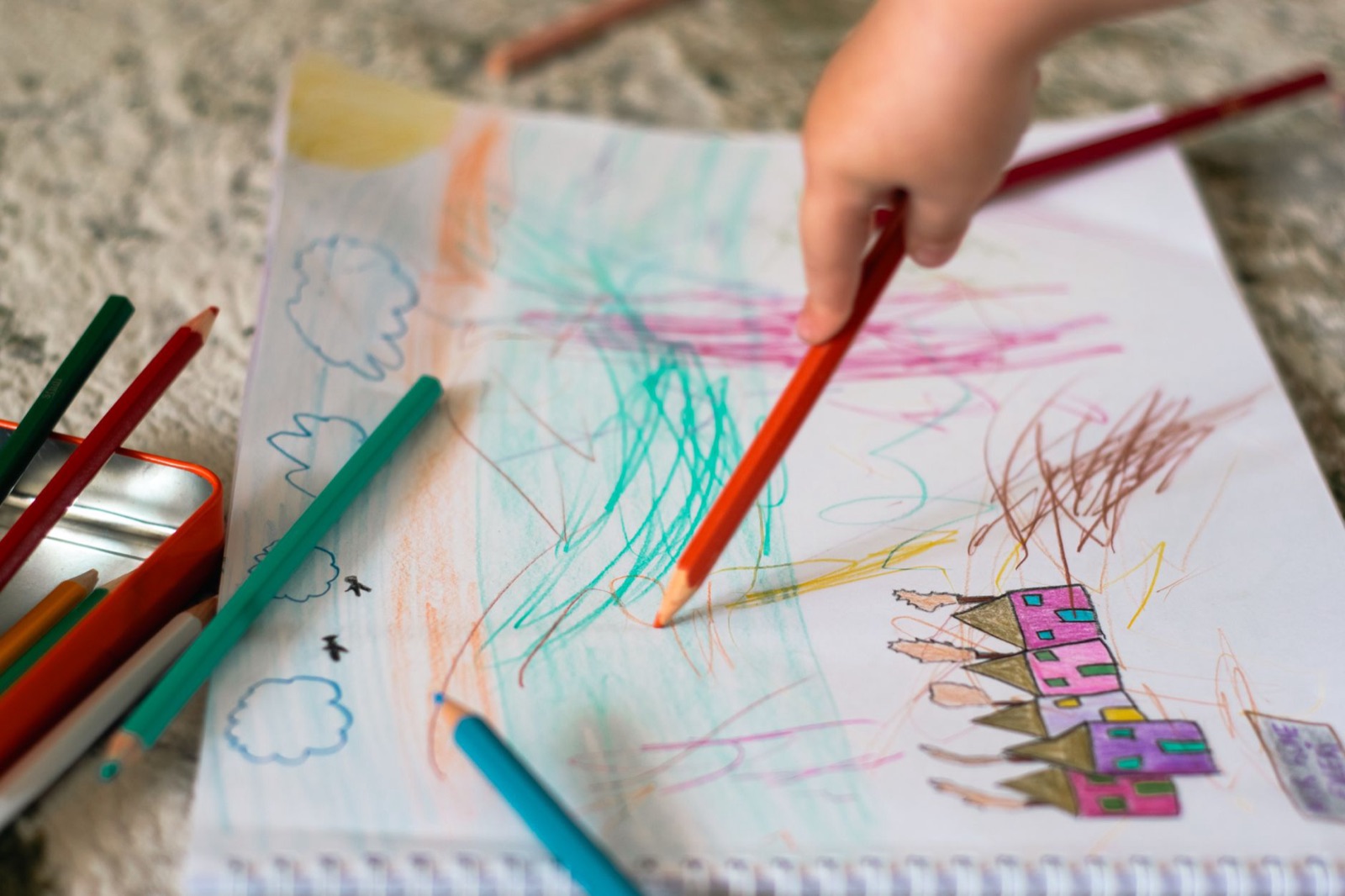 A child drawing with colored pencils on paper, showcasing creativity and imagination.