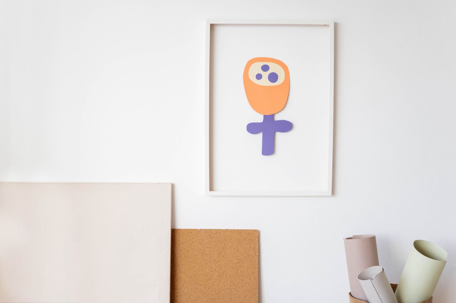 A child's colorful drawing in a frame with art supplies arranged on a minimalist indoor wall.
