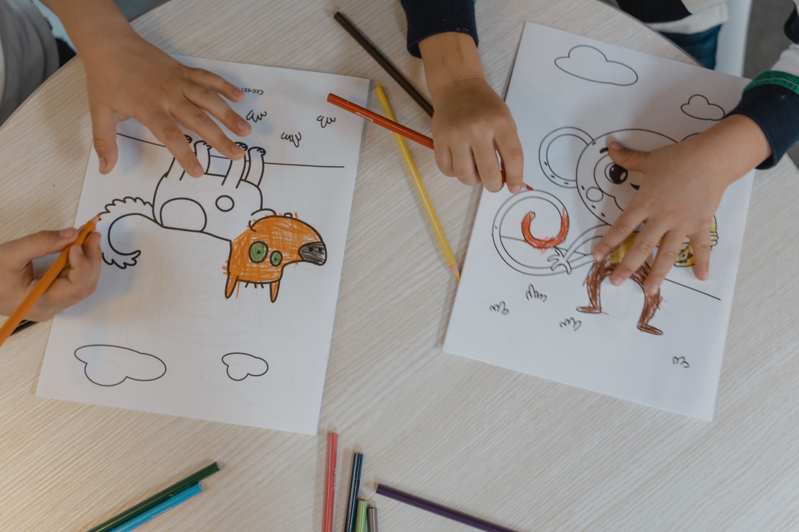 Children using colored pencils to bring animal drawings to life on a wooden table.